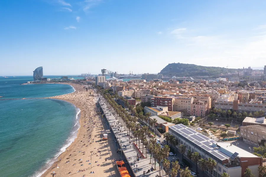 Barcelona from the air on a clear day: a long sandy beach curving beside turquoise sea, a palm-lined promenade and the city behind