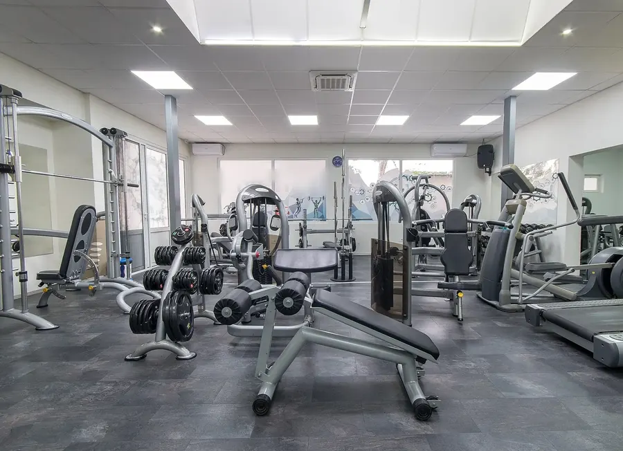 A bright, modern gym with grey slate floors, plate-loaded benches, a weight tree and cable machines under white ceiling lights