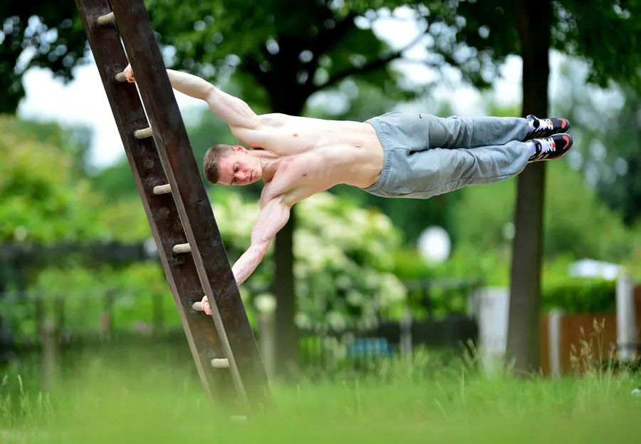 An athlete holds a human flag on a wooden ladder in a green park.